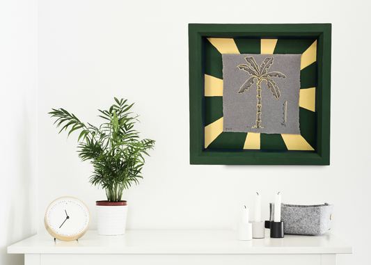 Decorative wall art with palm tree design on a white shelf with a plant and clock.