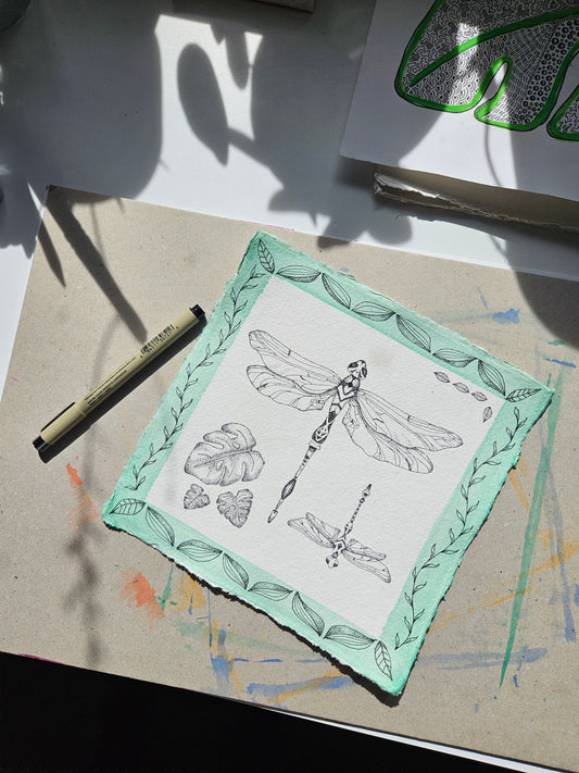 Hand-drawn dragonfly botanical illustration with tropical leaves and watercolour border, pen and ink on Khadi paper