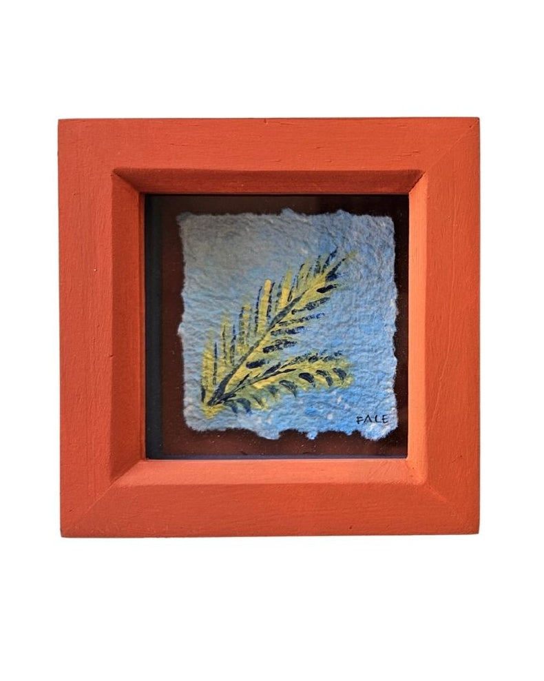 A square terracotta-colored wooden shadow box containing a textured blue tile with a palm leaf illustration, set against a plain white background.