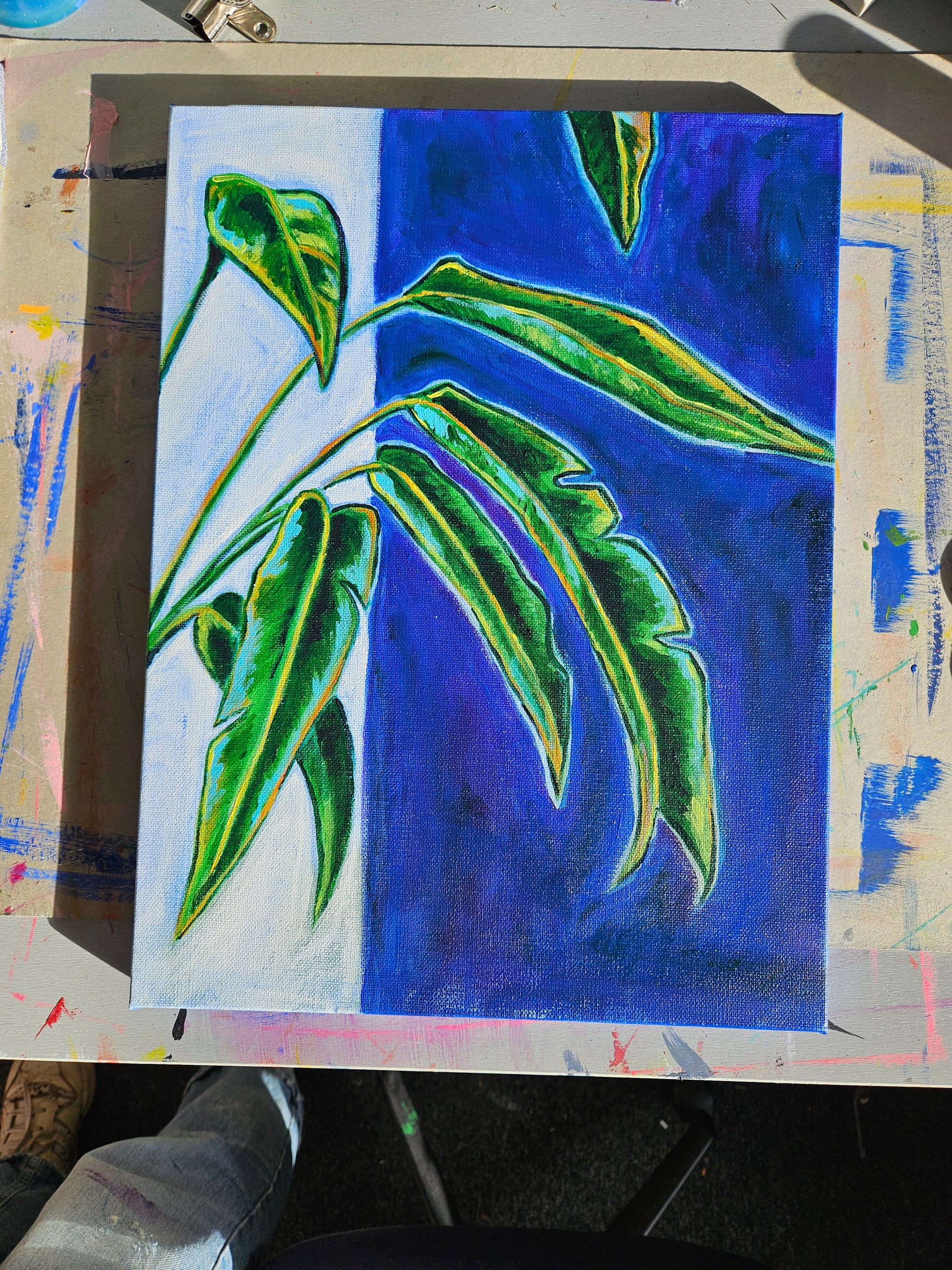 Painting of banana leaves on a blue background bathed in sunlight, on a desk