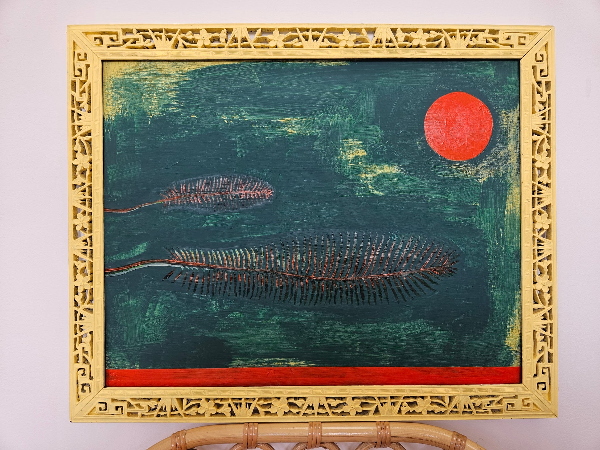 Two feathers in low contrast against a dark green background, with an orange sun and an orange stripe. Acrylic on wood. Handpainted ornate frame in pale yellow.