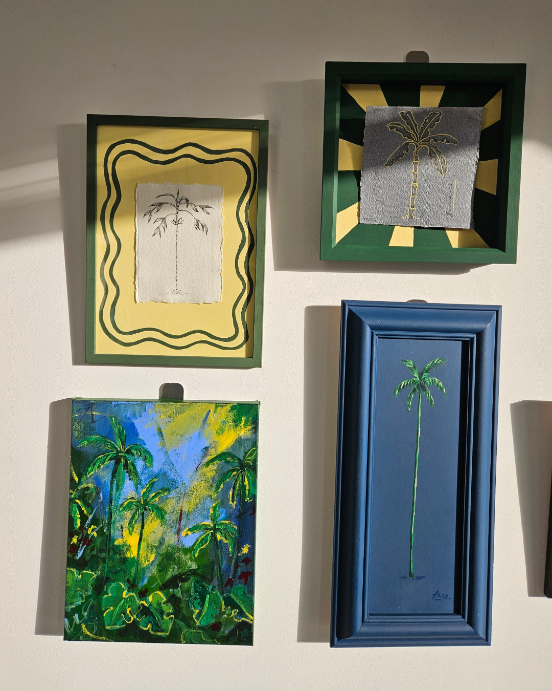 Four framed artworks with palm tree designs on a wall.