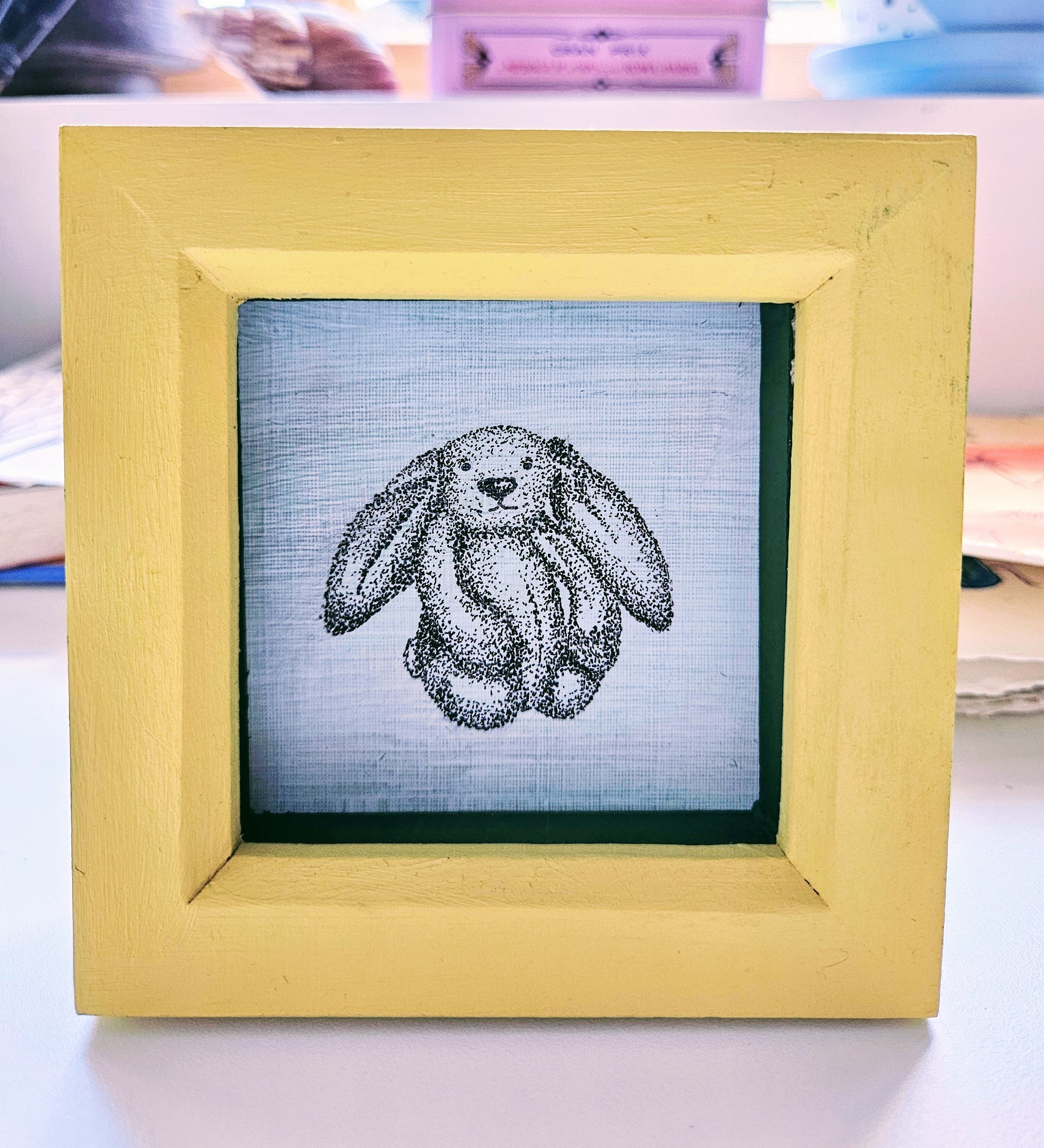 Pen and ink drawing of bunny toy, in a handpainted yellow and green box frame