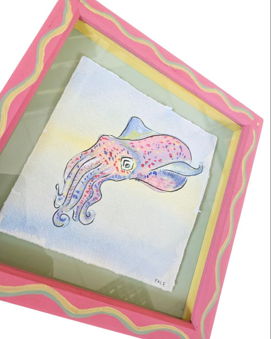 A framed watercolor painting of a pink and blue octopus on textured paper, set within a decorative pink and yellow wavy frame.