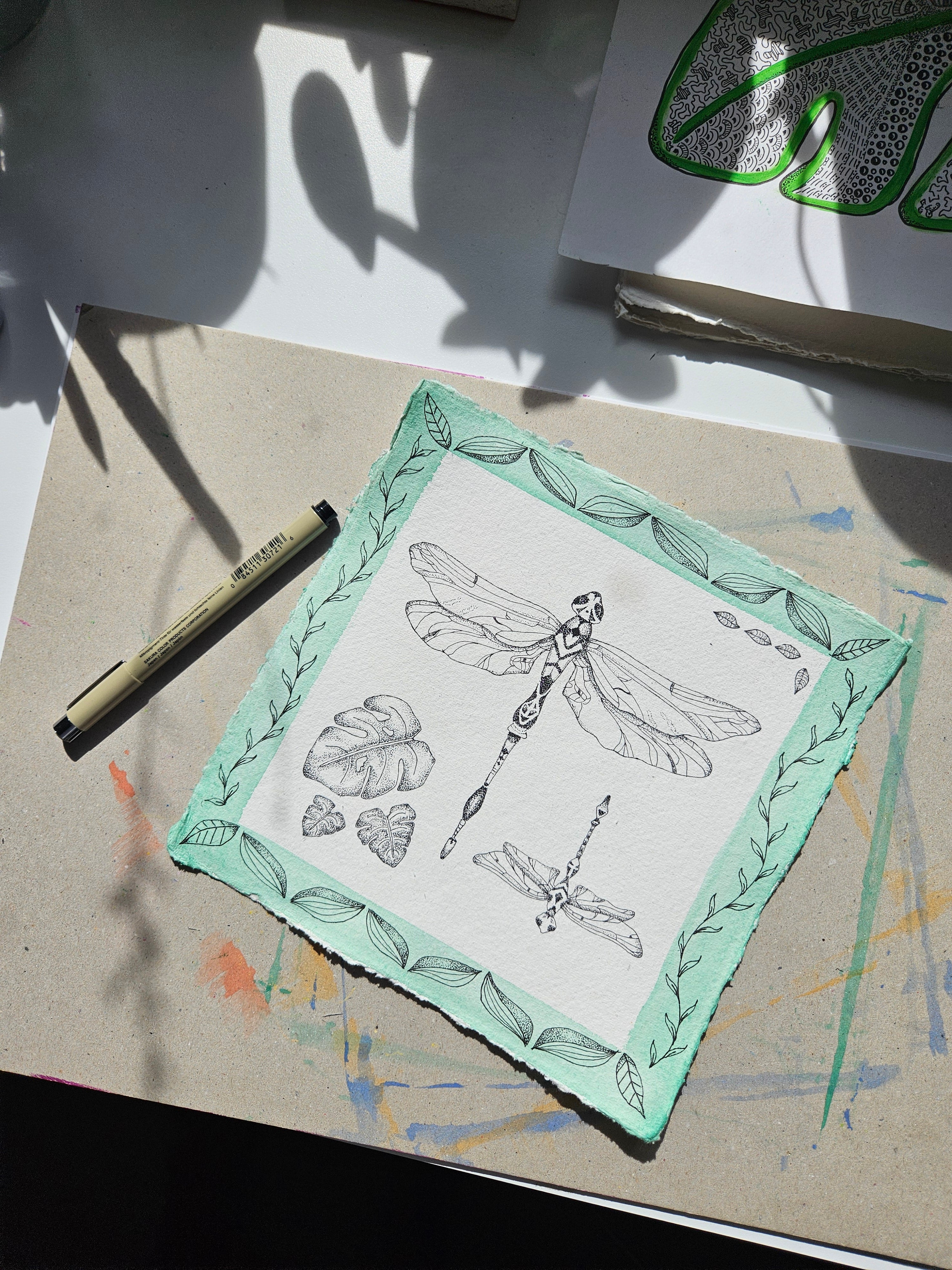 Hand-drawn dragonfly botanical illustration with tropical leaves and watercolour border, pen and ink on Khadi paper